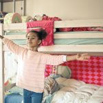 girl in white and red long sleeve shirt and blue denim jeans standing near bed