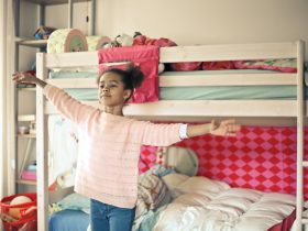 girl in white and red long sleeve shirt and blue denim jeans standing near bed